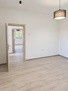 Empty room with light laminate flooring and open doors leading to other rooms. - image 4
