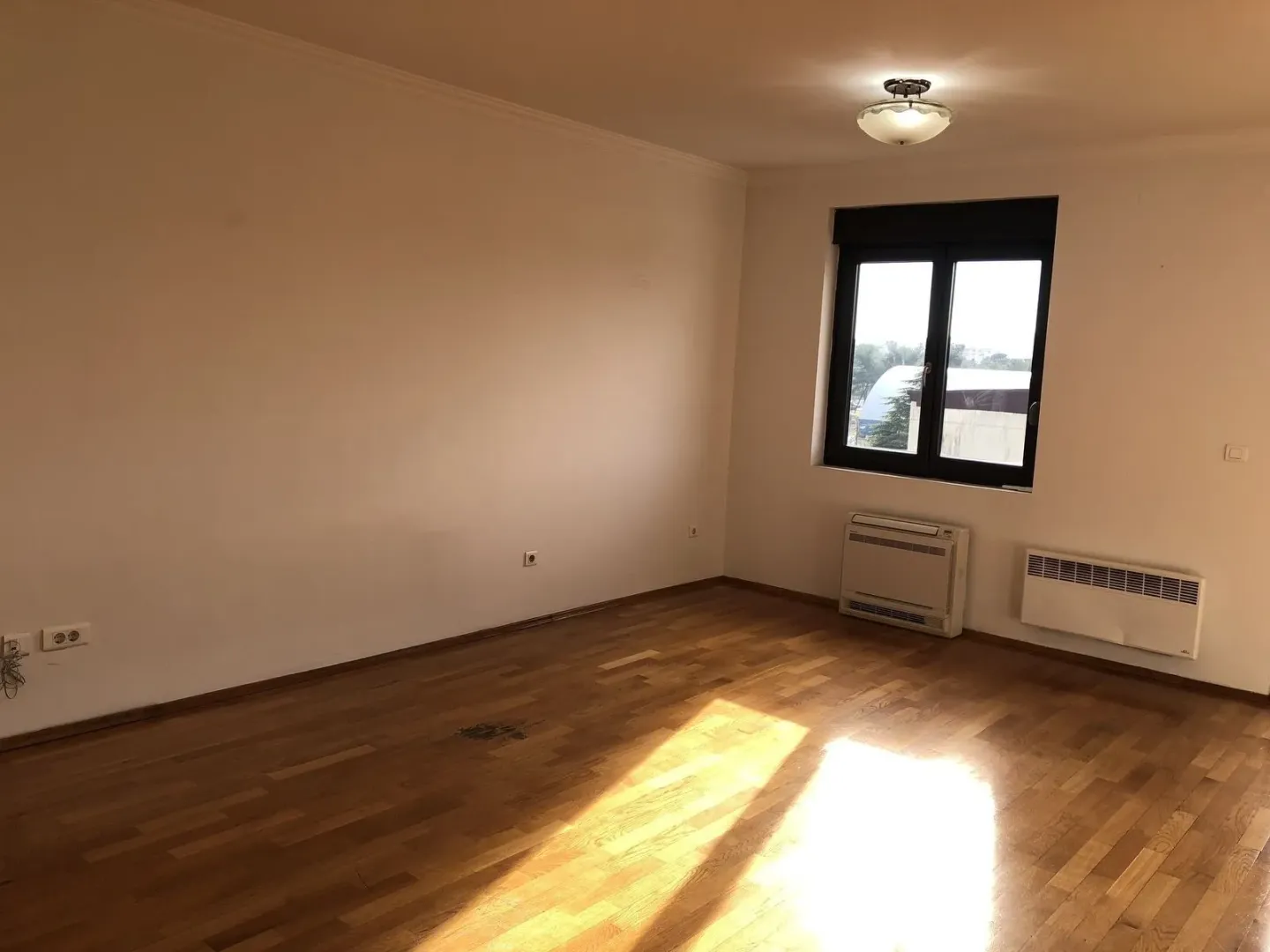 An empty room with parquet flooring and sunlight coming through a window.
