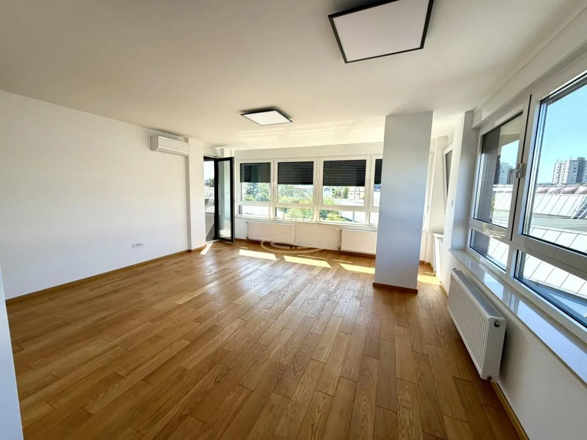 Empty living room with parquet flooring and large windows allowing plenty of natural light.