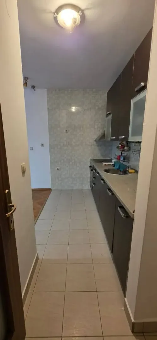 Pogled na usku kuhinju sa tamnim elementima i pločicama.