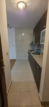 Pogled na usku kuhinju sa tamnim elementima i pločicama. - image 3