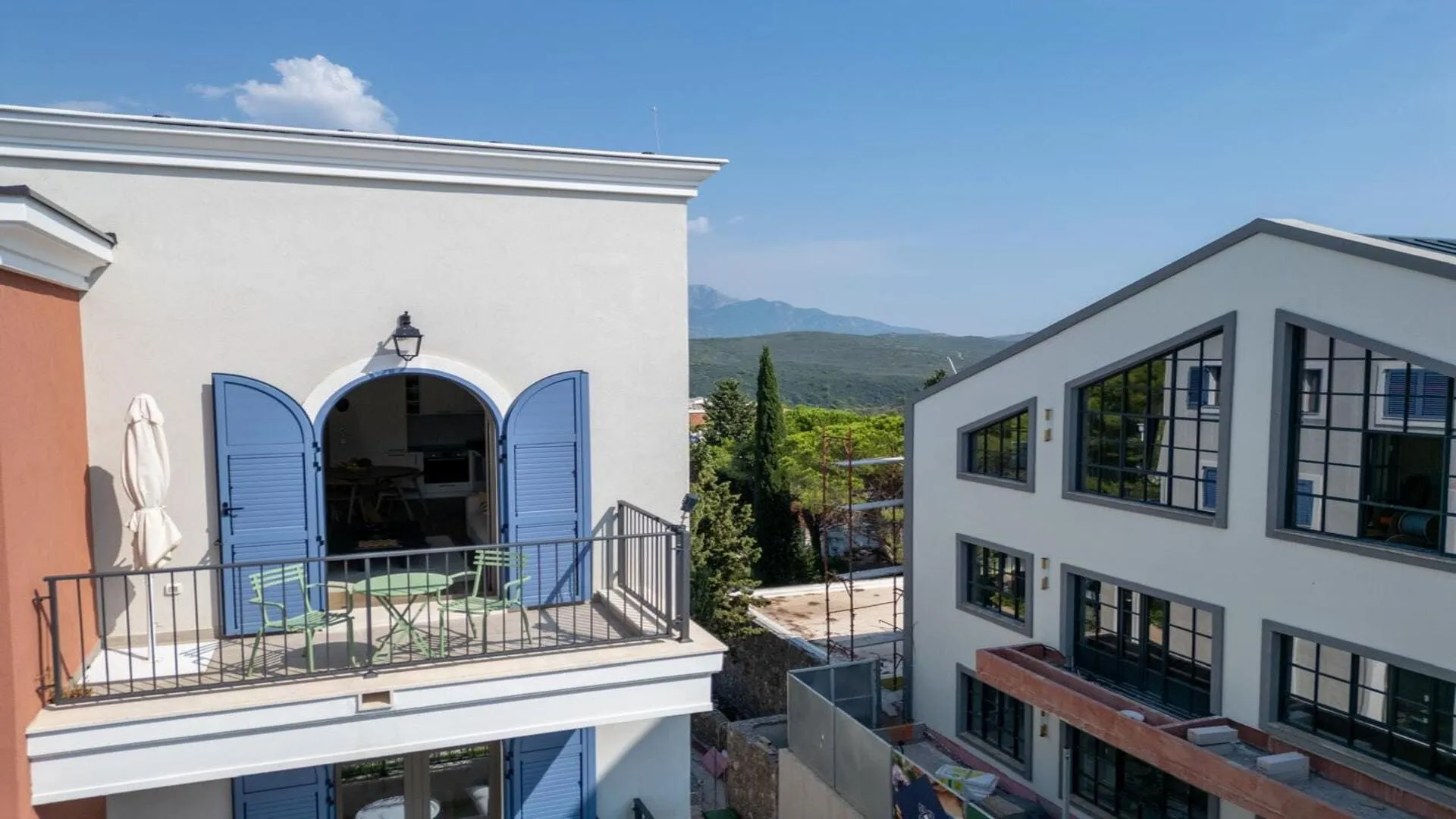 Pogled na spoljašnjost zgrade sa balkonom i plavim žaluzinama.