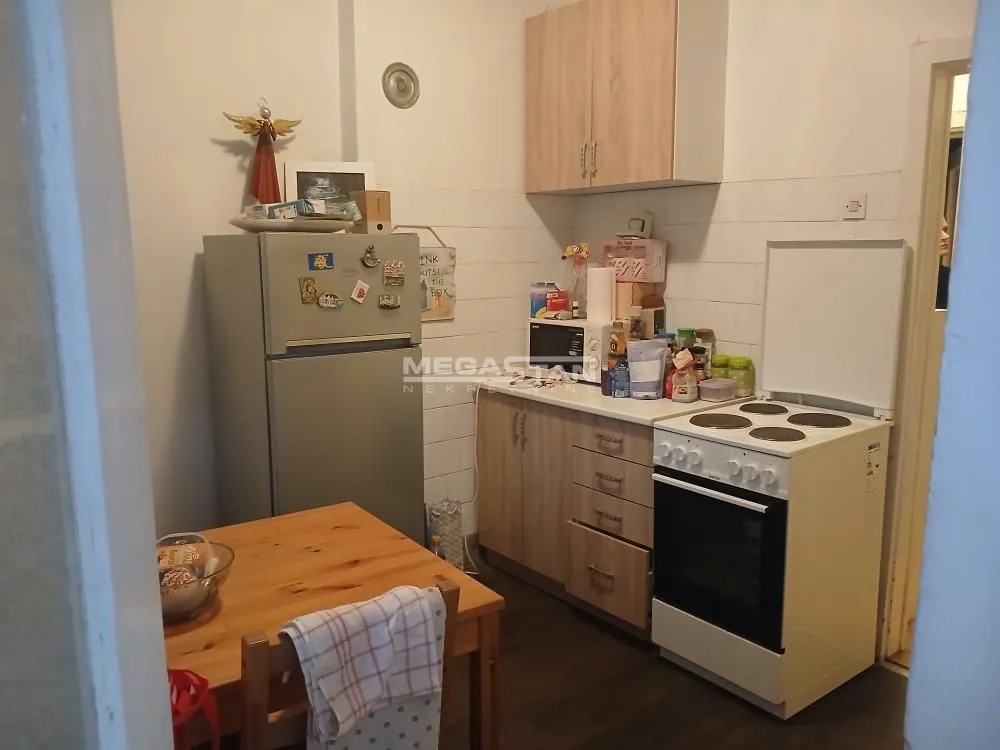 Manja kuhinja sa drvenim elementima, frižiderom i trpezarijskim stolom.