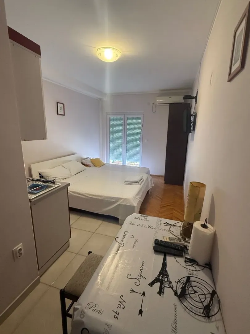 Manja spavaća soba sa bračnim krevetom, kuhinjskim elementima i trpezarijskim stolom.