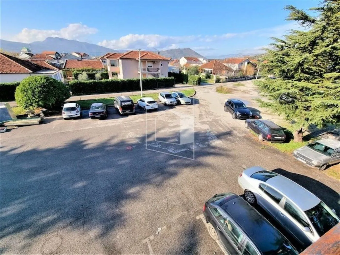 View from the terrace of a parking lot and surrounding houses with hills in the background.