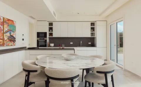 Moderna kuhinja sa bijelim elementima i okruglim trpezarijskim stolom. - image 6