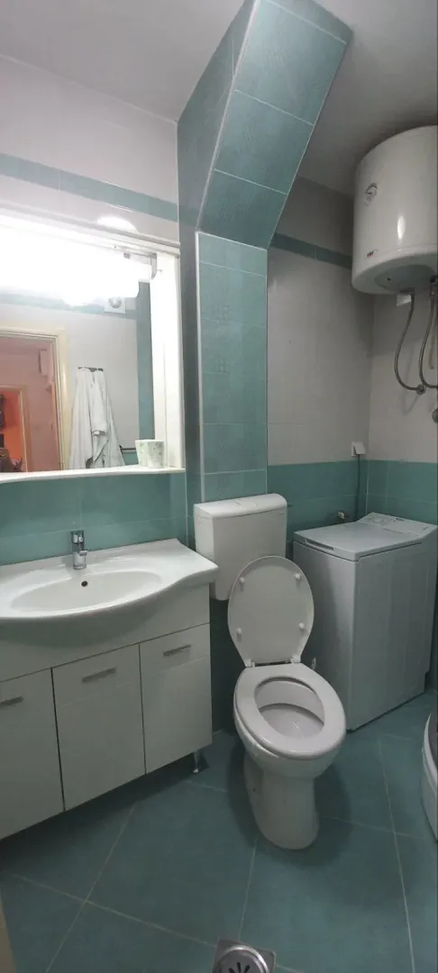 A simple bathroom featuring a sink, mirror, toilet, and washing machine.