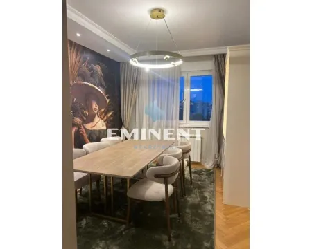 Dining room with a wooden table, chairs, and decorative wallpaper on the wall. - image 4