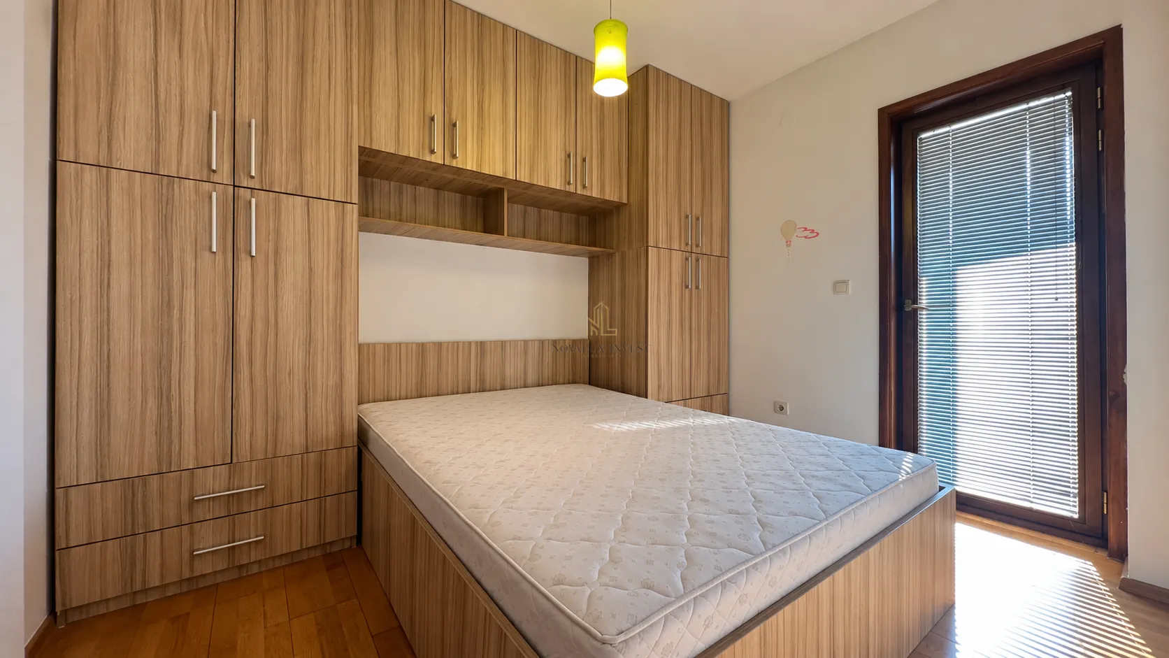 Spavaća soba sa ugradnim drvenim plakarima oko kreveta i izlazom na terasu.