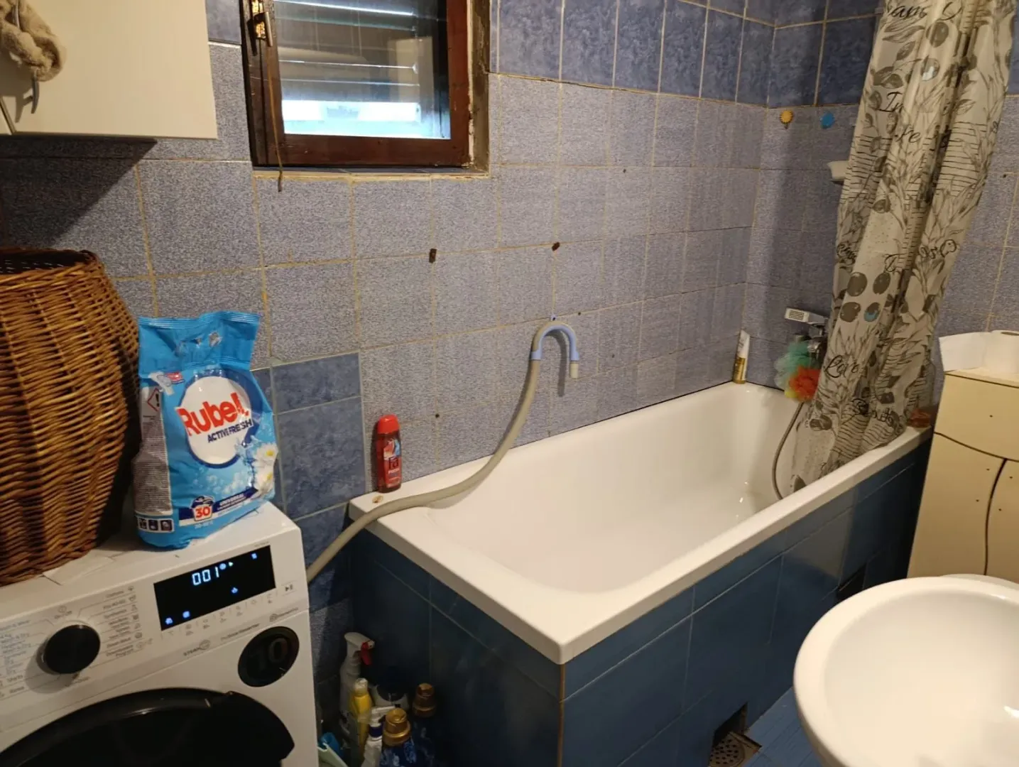 Manje opremljeno kupatilo sa kadom, plavim pločicama i mašinom za veš.