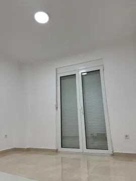 An empty room with light floor tiles and white balcony doors. - image 6
