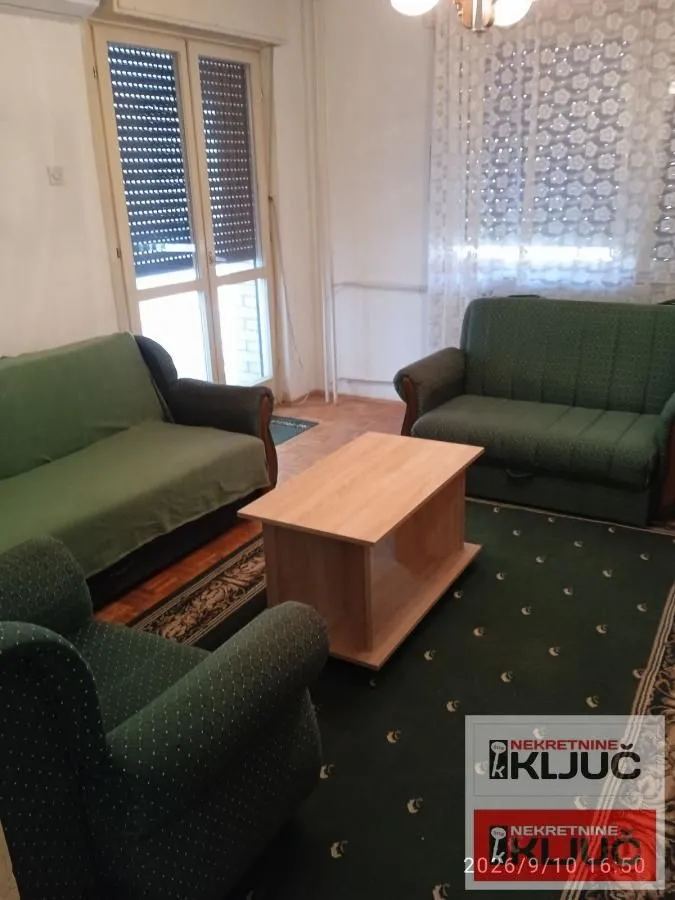 Dnevna soba sa garniturom za sedenje, stočićem i balkonskim vratima.