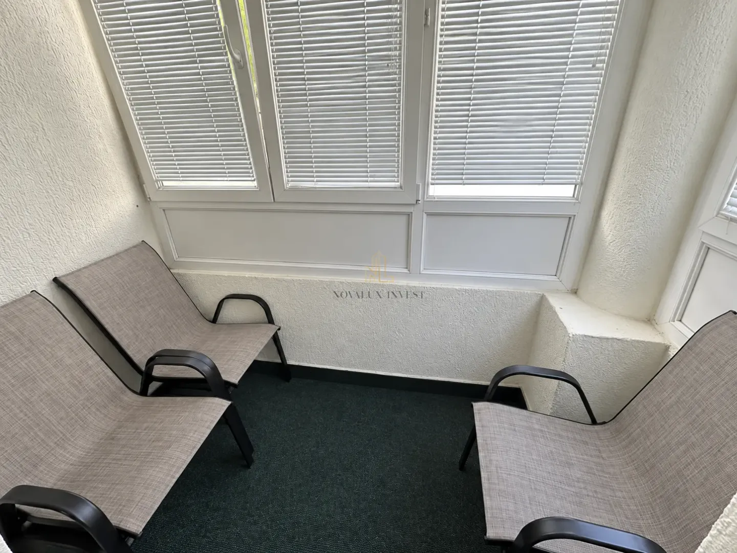 Enclosed balcony space with three chairs and window blinds.
