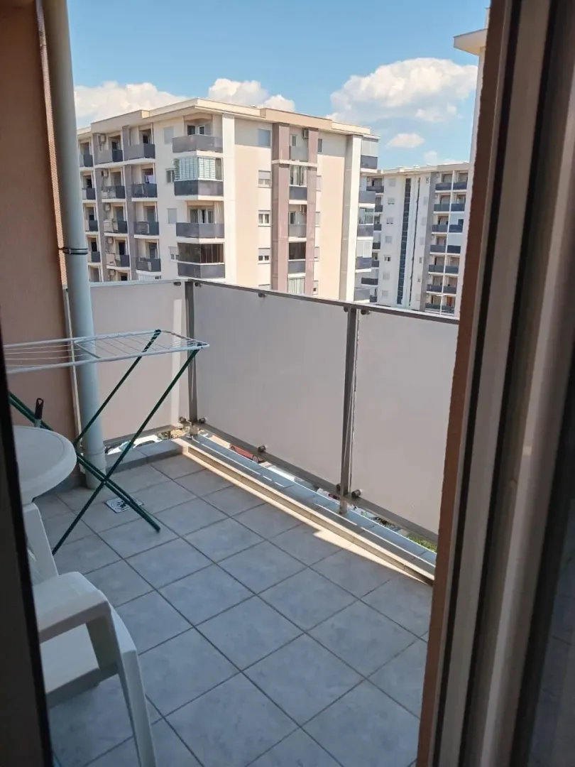Manji popločani balkon sa ogradom i pogledom na okolne zgrade.