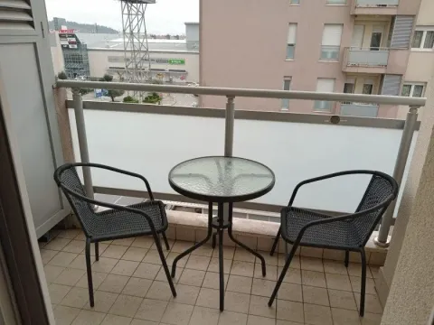 Manji namješteni balkon sa stočićem i dve stolice i pogledom na okolne zgrade. - image 8