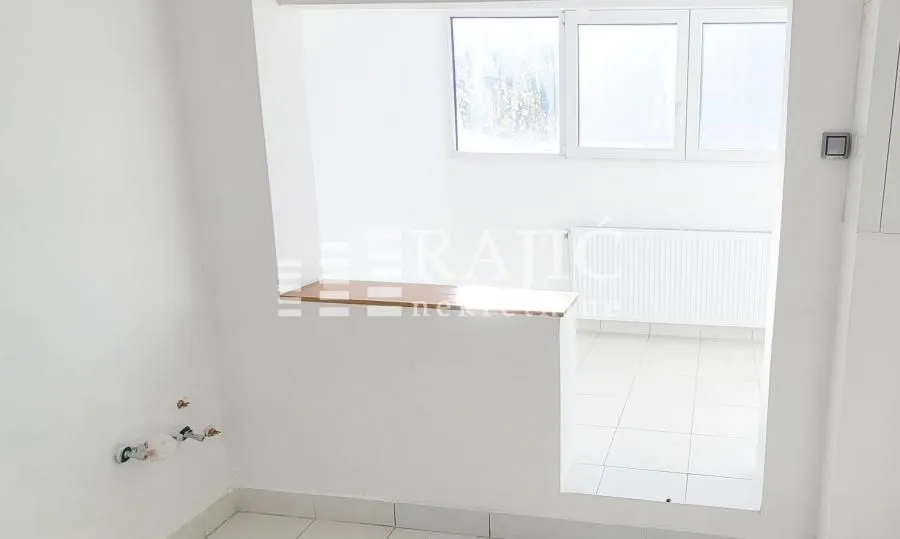 Pogled na kuhinjski prostor sa šankom i belim pločicama.