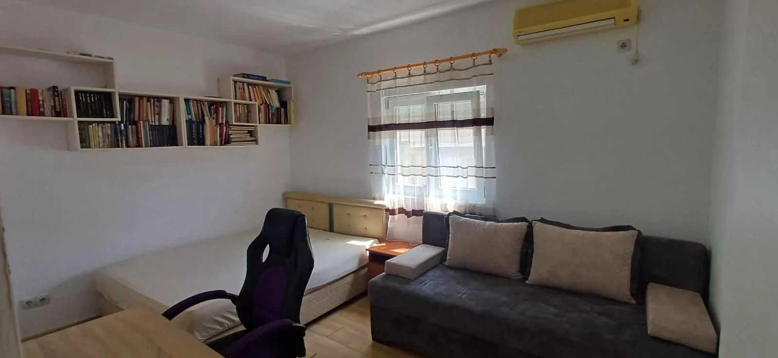 Smaller bedroom with a bed, sofa, desk, and wall bookshelf.