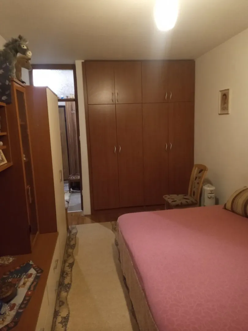Spavaća soba sa velikim drvenim ormarom i krevetom sa roze prekrivačem.