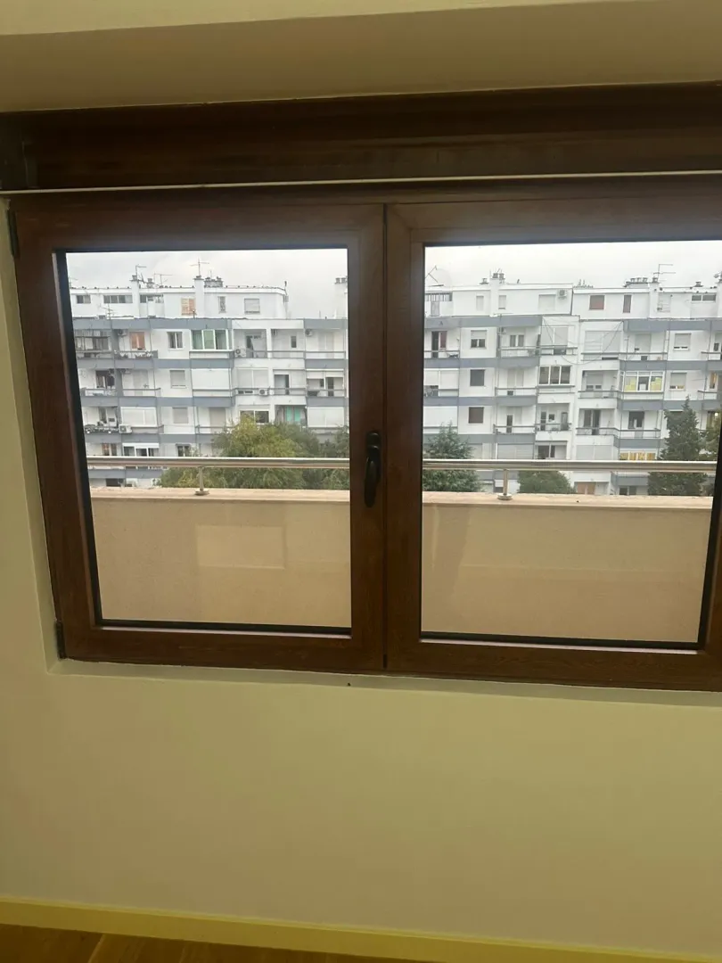 A view through a wood-framed window showing a balcony and neighboring residential buildings.