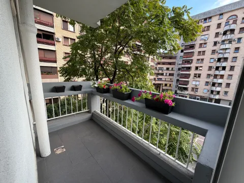 Manji uređeni balkon sa ogradom i saksijama cvijeća, sa pogledom na zgrade i drveće. - image 10