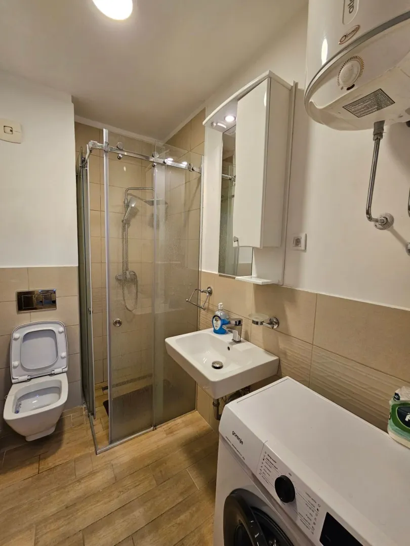 Compact bathroom with a shower cabin, washbasin, and washing machine.