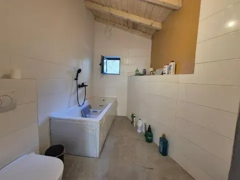 Manje kupatilo sa kadom, toaletom i drvenim gredama na plafonu. - image 3