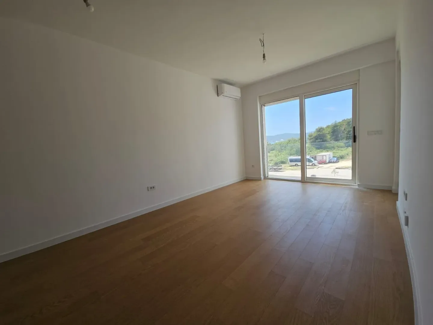 Prazna soba sa drvenim podom i velikim balkonskim vratima.