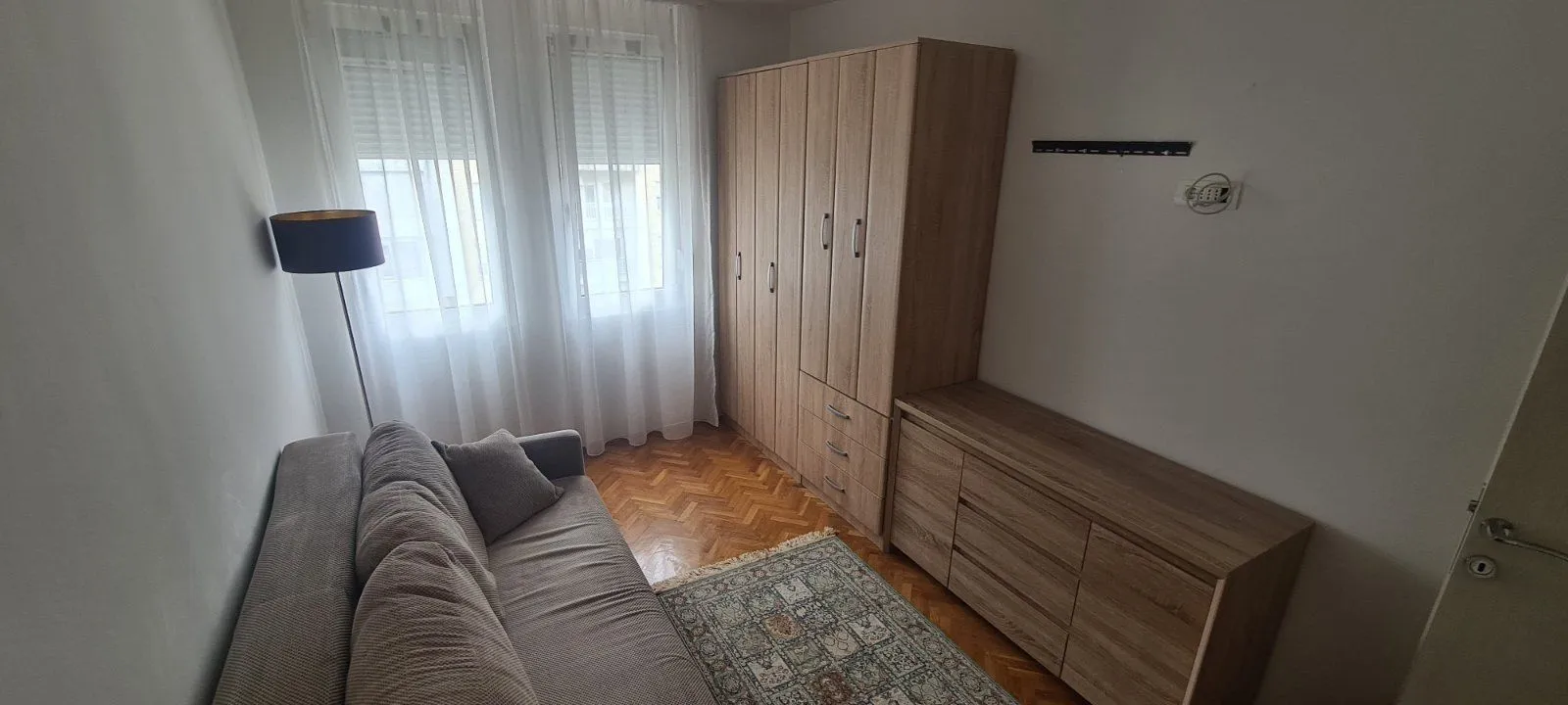 Svijetla soba sa kaučem, drvenim ormarom, komodom i tepihom.