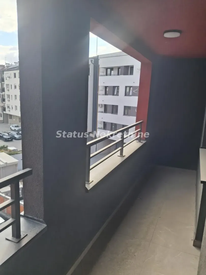 Natkriveni balkon sa metalnom ogradom i pogledom na susedne zgrade.