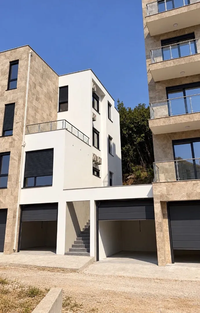 Spoljašnji izgled moderne stambene zgrade sa garažnim prostorom i balkonima.