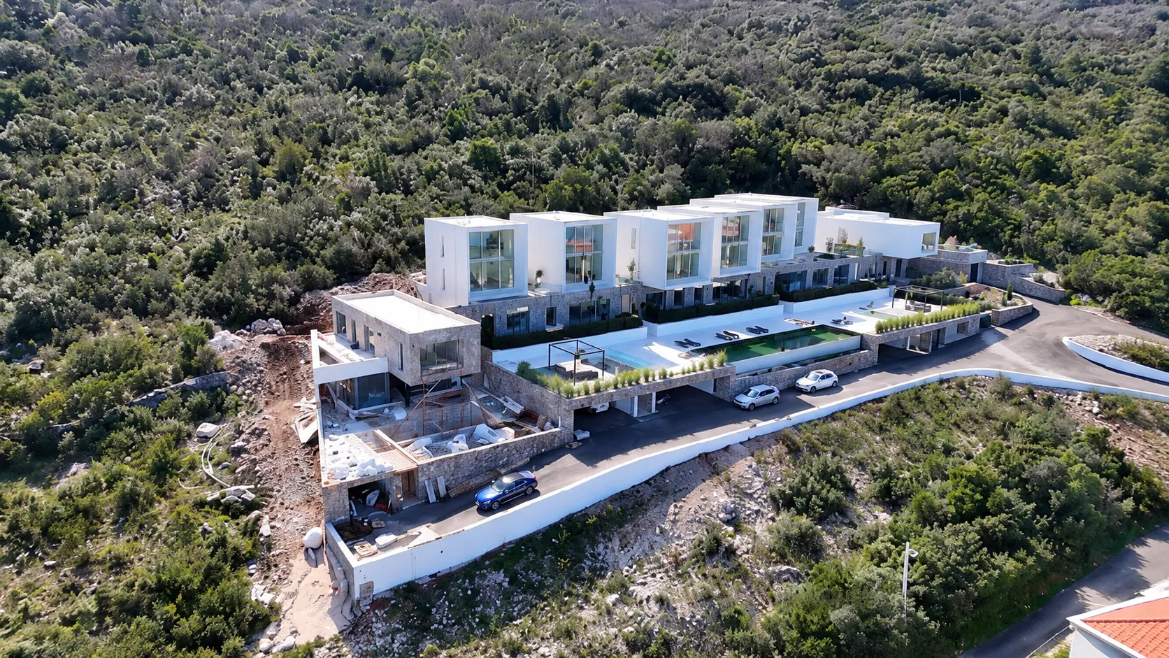 Pogled iz vazduha na kompleks modernih vila sa bazenima okruženih šumom.