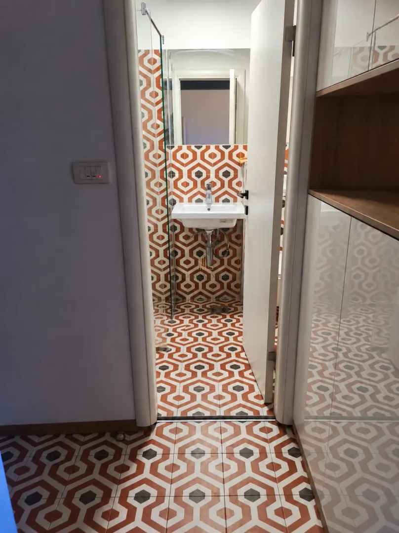 Pogled iz hodnika na kupatilo sa upečatljivim geometrijskim pločicama i umivaonikom.
