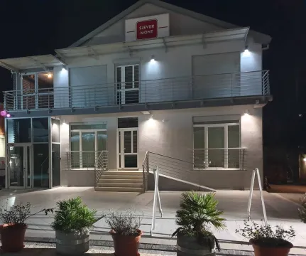Exterior view of a two-story building illuminated at night with a paved courtyard and potted plants. - image 21