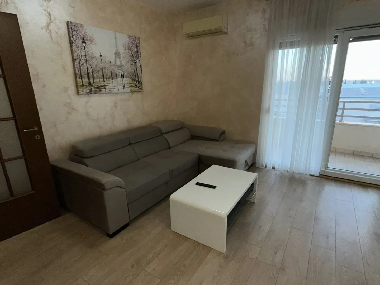 Dnevni boravak sa sivom ugaonom garniturom, klub stolom i izlazom na balkon.