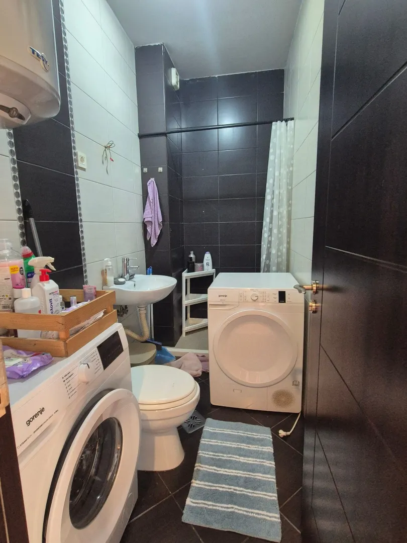 Compact bathroom with a washing machine, washbasin, and shower area with a curtain.