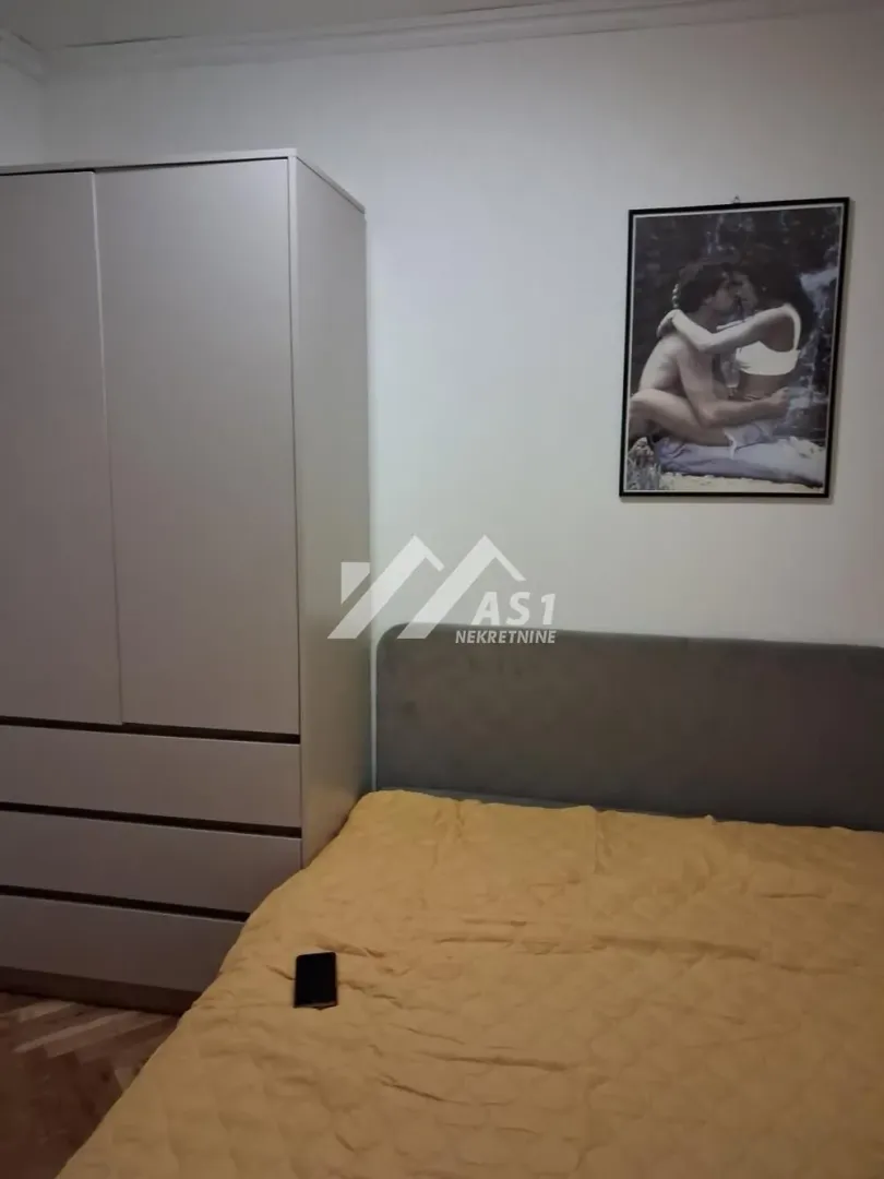 Spavaća soba sa bračnim krevetom, garderoberom i zidnom slikom.