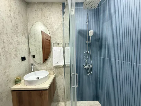 Moderno kupatilo sa tuš kabinom, lavaboom i okruglim ogledalom. - image 9