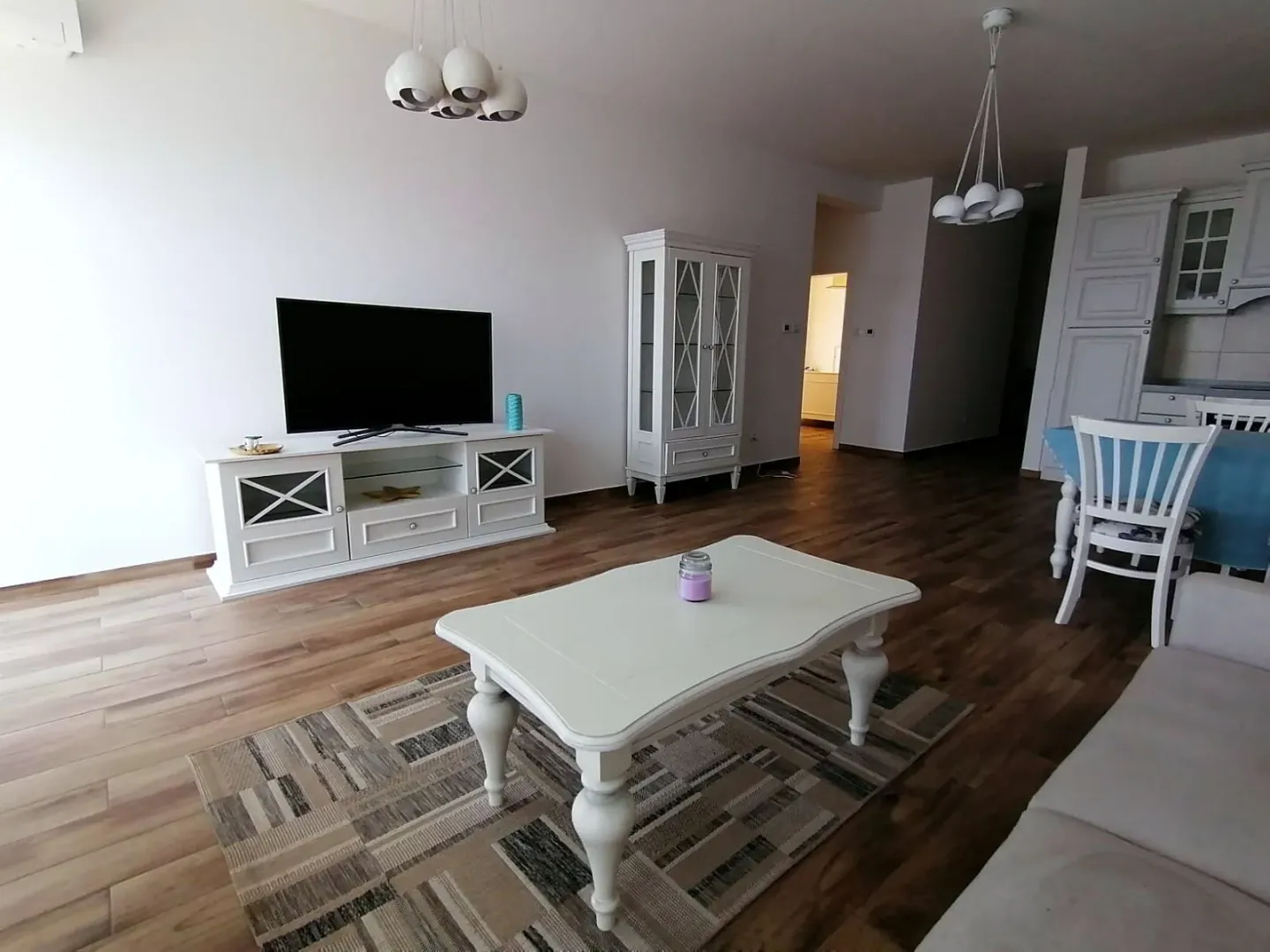 Dnevna soba sa garniturom, TV komodom i trpezarijskim dijelom u pozadini.