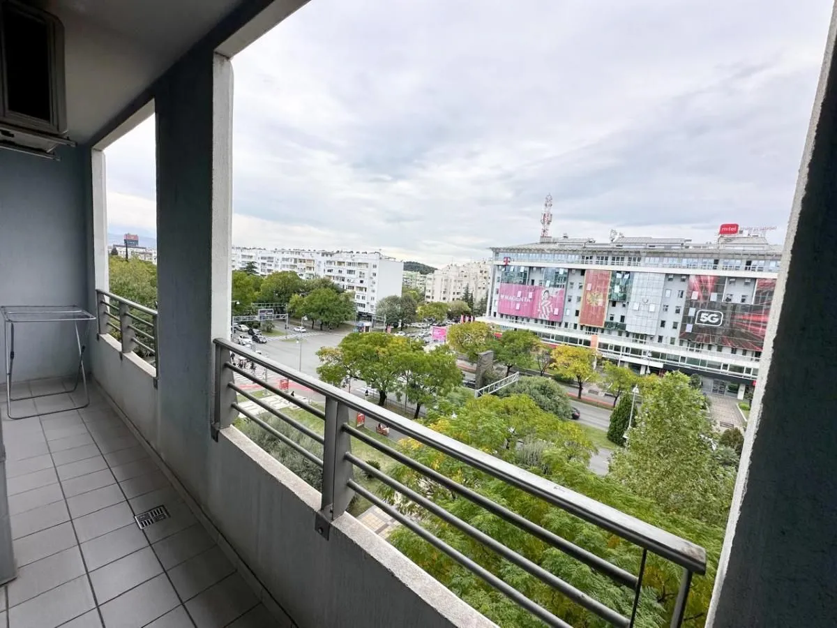 Dugačak natkriveni balkon sa metalnom ogradom i pogledom na gradsku ulicu i zgrade.