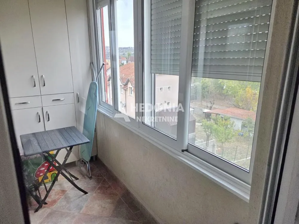 Zastakljeni balkon sa ugradnim ormarom i pogledom na naselje.