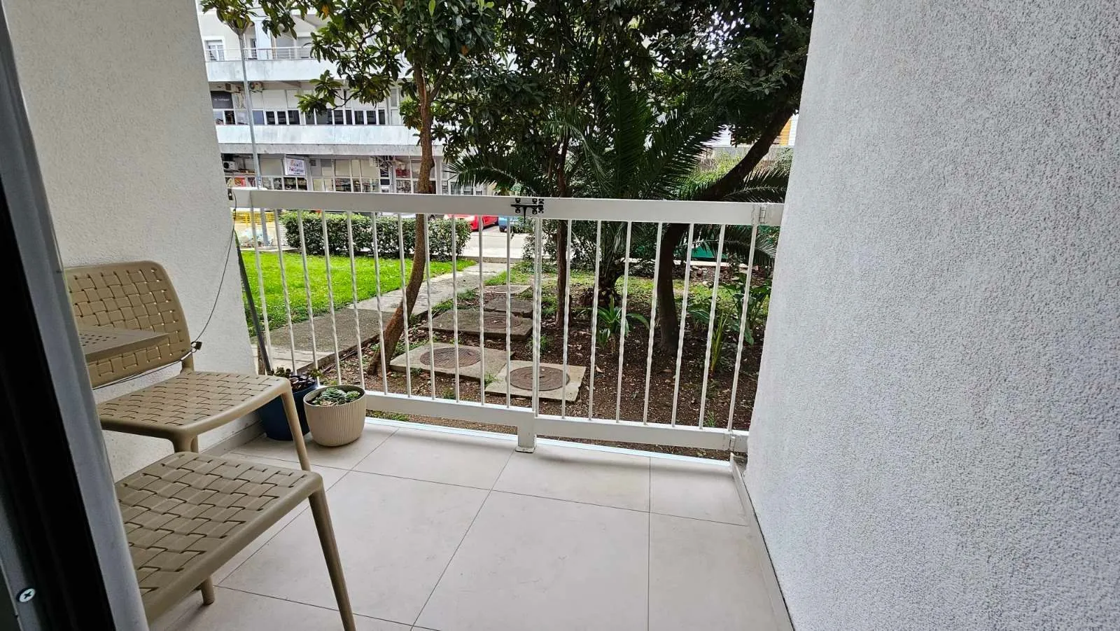 Manji popločani balkon sa stolicama i pogledom na dvorište i zelenilo.