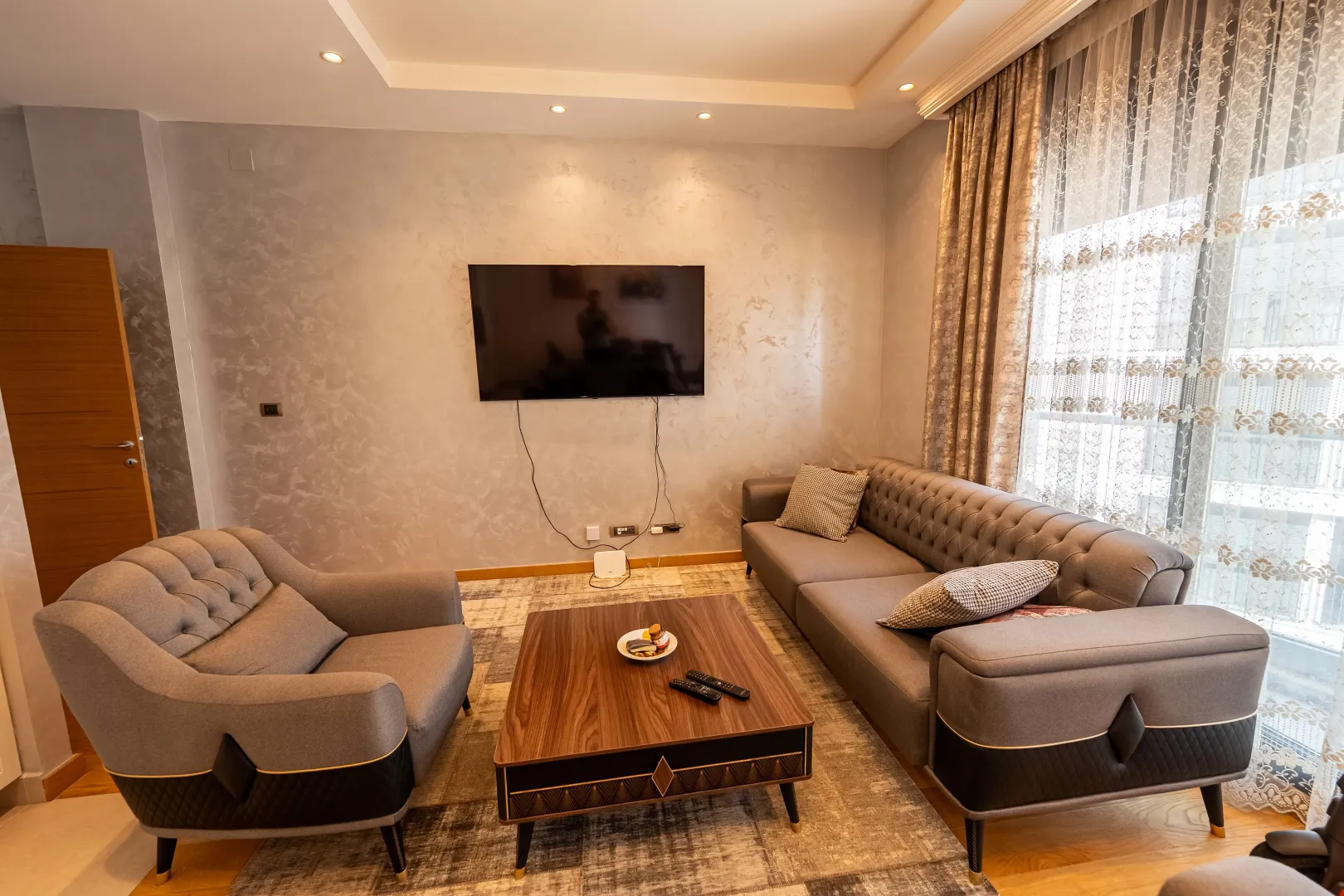 Living room with a grey sofa set, armchair, and a wall-mounted TV.