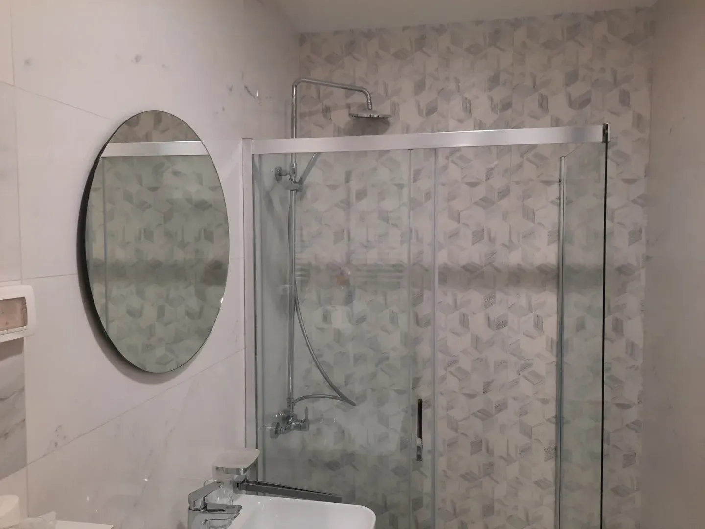 Modern bathroom with a glass shower cabin, a round mirror, and a sink.