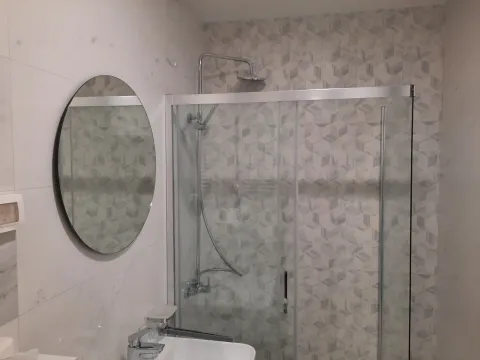 Modern bathroom with a glass shower cabin, a round mirror, and a sink. - image 8