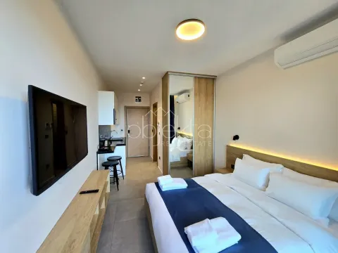 Master bedroom with a double bed, TV, and a small kitchen in the background. - image 8