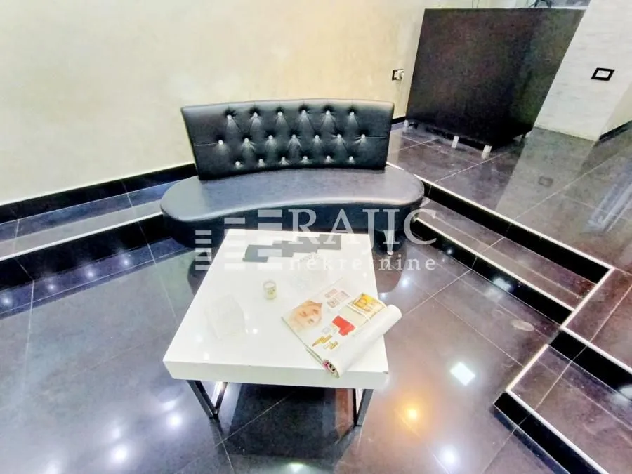 Living room with a black upholstered sofa and a white coffee table on glossy tiles.