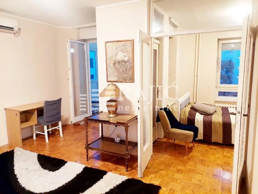 Living room with parquet flooring and a view into the bedroom.