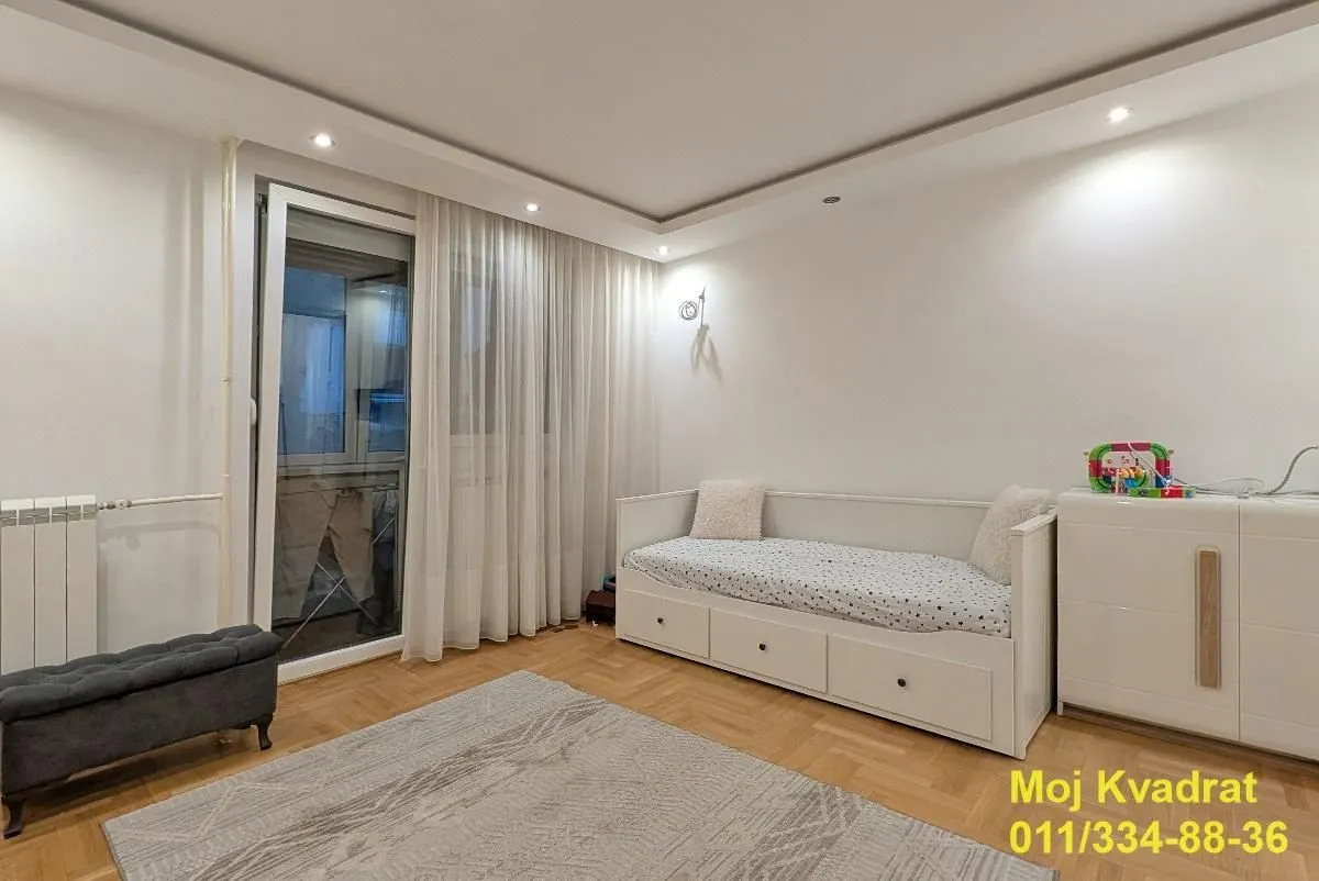 Dečja soba sa krevetom, belom komodom i izlazom na terasu.