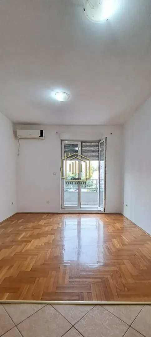 Prazna soba sa parketom i izlazom na balkon.
