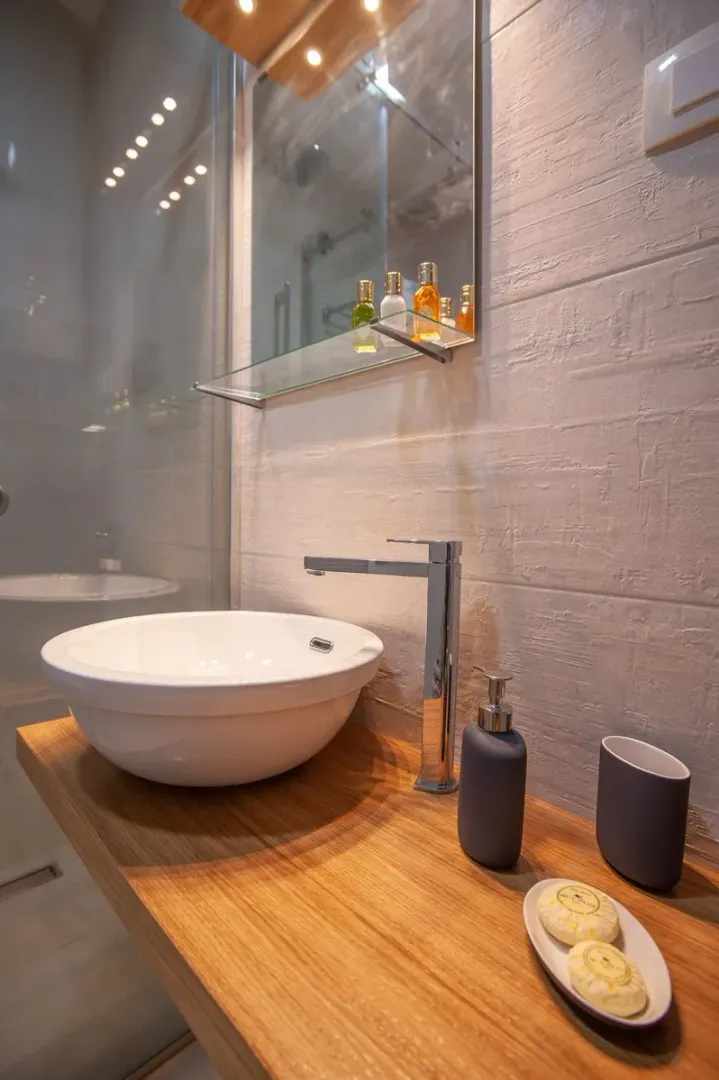 Modern washbasin on a wooden vanity with a mirror and a shower cabin.